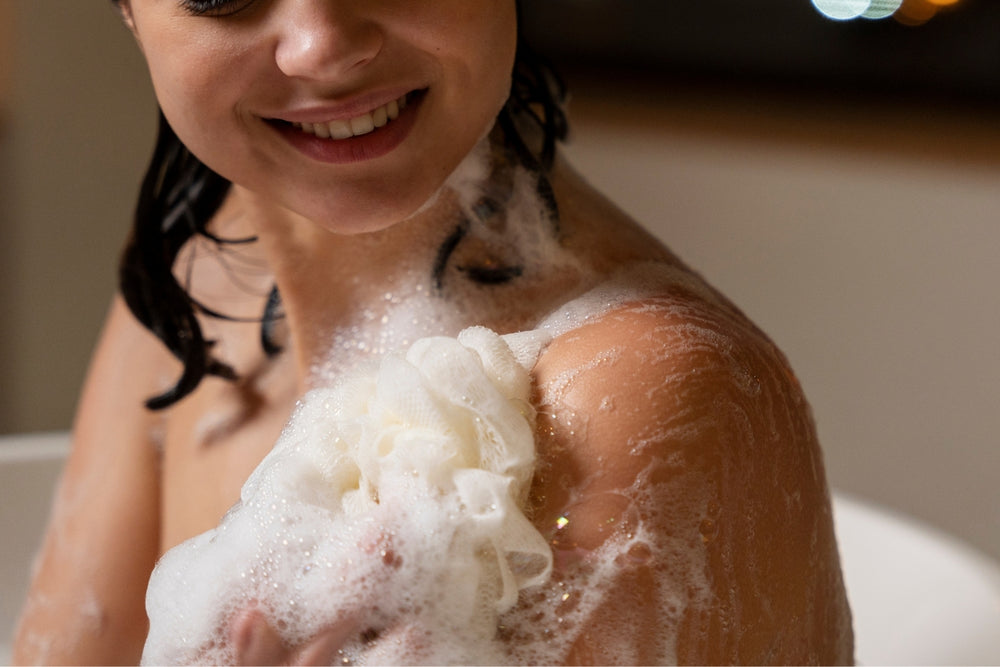Woman washing her shoulder with a lathered bath sponge.