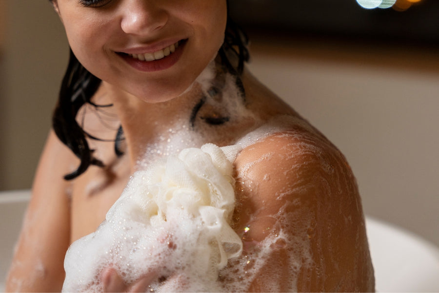 Woman washing her shoulder with a lathered bath sponge.
